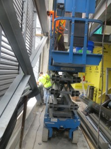 A hard-wheeled lift is used to access higher reaches of the roof enclosure without benefit of protection of the membrane. Workers are welding over the unprotected membrane—an activity that resulted in holes in the membrane from weld spatter. 