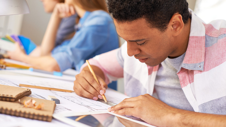 Portrait of young engineer making sketch with other designers on background