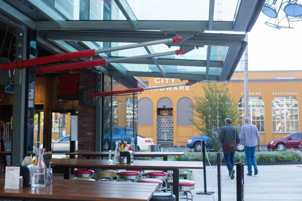 The glass-clad hydraulic doors at Sam’s Tavern provide a protective canopy for outside diners. Photos by Schweiss Doors