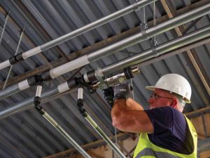 Plumber using PEX expansion/compression tool to form secure connections in commercial project. Also shown are galvanized steel support channels and support hangers.