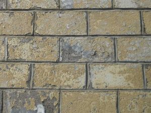 This mid-20th century concrete masonry commercial building had always been coated. A recent repair campaign included stripping of many layers of coating buildup, reconstruction of cracked and displaced masonry, and repointing of mortar joints (work in progress in this view). After all masonry repair work had been completed and inspected, a new elastomeric, breathable coating system was applied.