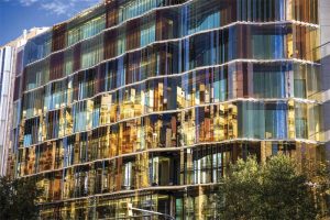 Vertical laminated glass panels featuring PVB interlayers in multiple colors shine under the sun’s rays and offer dazzling reflections of buildings that surround  the EADA Business School in Barcelona, Spain. Photo © Jose Masterton