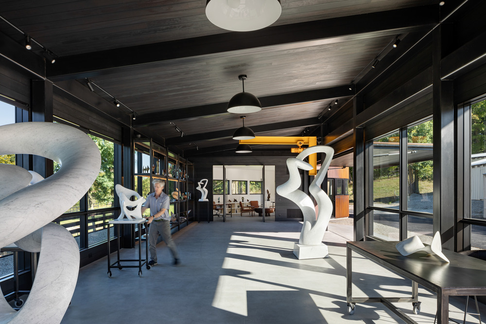 The artist in studio. In the background, the monumental steel shelving is visible. The interior wall and ceiling finishes are black to contrast with the marble sculptures.