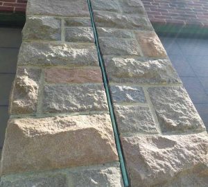 Vertical copper sheet metal expansion joint in a historic stone masonry wall.