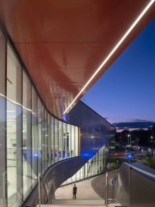 Standing atop the exterior stairway, underneath the cantilevered third floor terrace, featuring a metal accent, looking along the north facade.