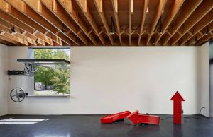 Gallery space maximizes flexibility with a large pivoting window. Wood rafters are seen in the ceiling of the space.