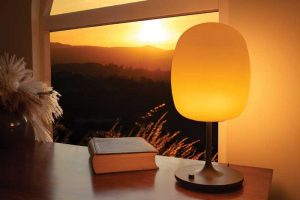 A wellness lamp on a table next to a room window with a sunset view.