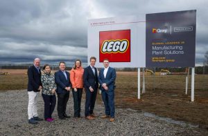 LEGO representatives pose with general contractor representatives, with the new manufacturing plant's site in the background.