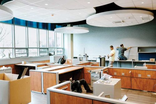 Men working on creating the interior of a classroom, with some suspended HVAC installations hanging from the ceiling.