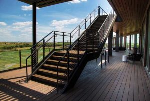 Here a high-grade stainless steel is used in a cable railing for a staircase in a recreational building. The staircase leads from a lower-level wooden deck onto a higher-level deck.