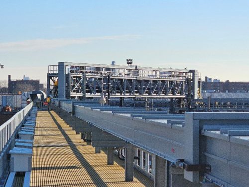 A steel truss bridge at Coney Island Yard, with subway tracks in the foreground and city skyline in the distance.