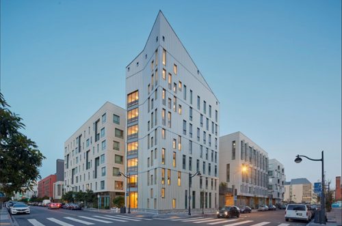 Modern triangular white building on a city street corner at dusk.