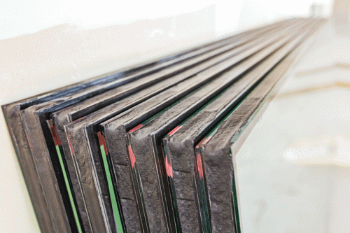 Close-up view of multiple glass panels with edge seals neatly stacked together. The seals and layers of the glass are clearly visible, highlighting the precision of the manufacturing process.