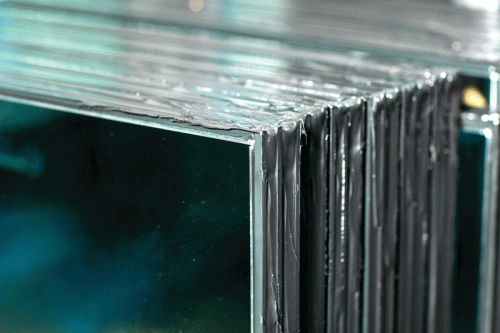 Close-up of stacked glass panels with protective sealant applied along the edges, highlighting the finishing process in glass manufacturing.