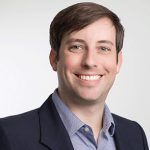 Headshot of Ryan Stoltz smiling, in a black suit.