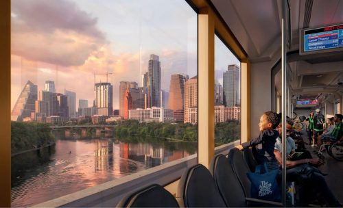 A modern train interior with passengers seated and standing, including a child looking out the window. The view outside showcases a vibrant city skyline with tall buildings, a bridge, and a calm river at sunset. The atmosphere inside the train is casual, with people engaged in various activities. A screen displays upcoming station information.