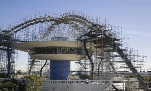 Iconic building under renovation with extensive scaffolding, featuring a futuristic circular design supported by a central column, set against a clear blue sky.