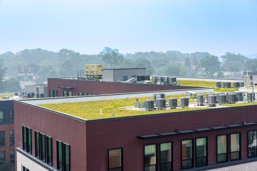 Rooftop with grass and HVAC units on a multi-story building, surrounded by suburban landscape under a hazy sky.