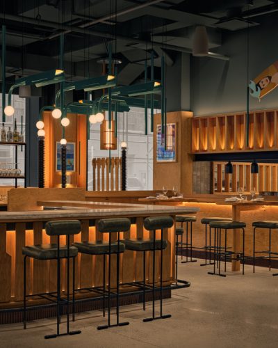 Modern bar interior with wooden features, green pendant lights, and seating.