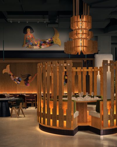 Modern restaurant interior featuring wooden furniture, colorful mermaid artwork, and unique lighting.