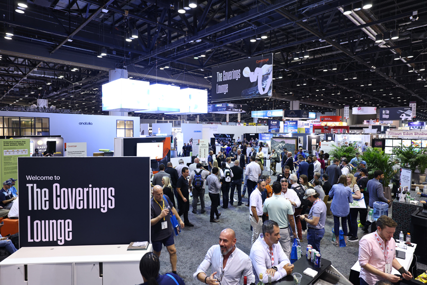 A busy convention hall with people mingling near a sign reading "Welcome to The Coverings Lounge." Stands and displays surround the lively crowd.